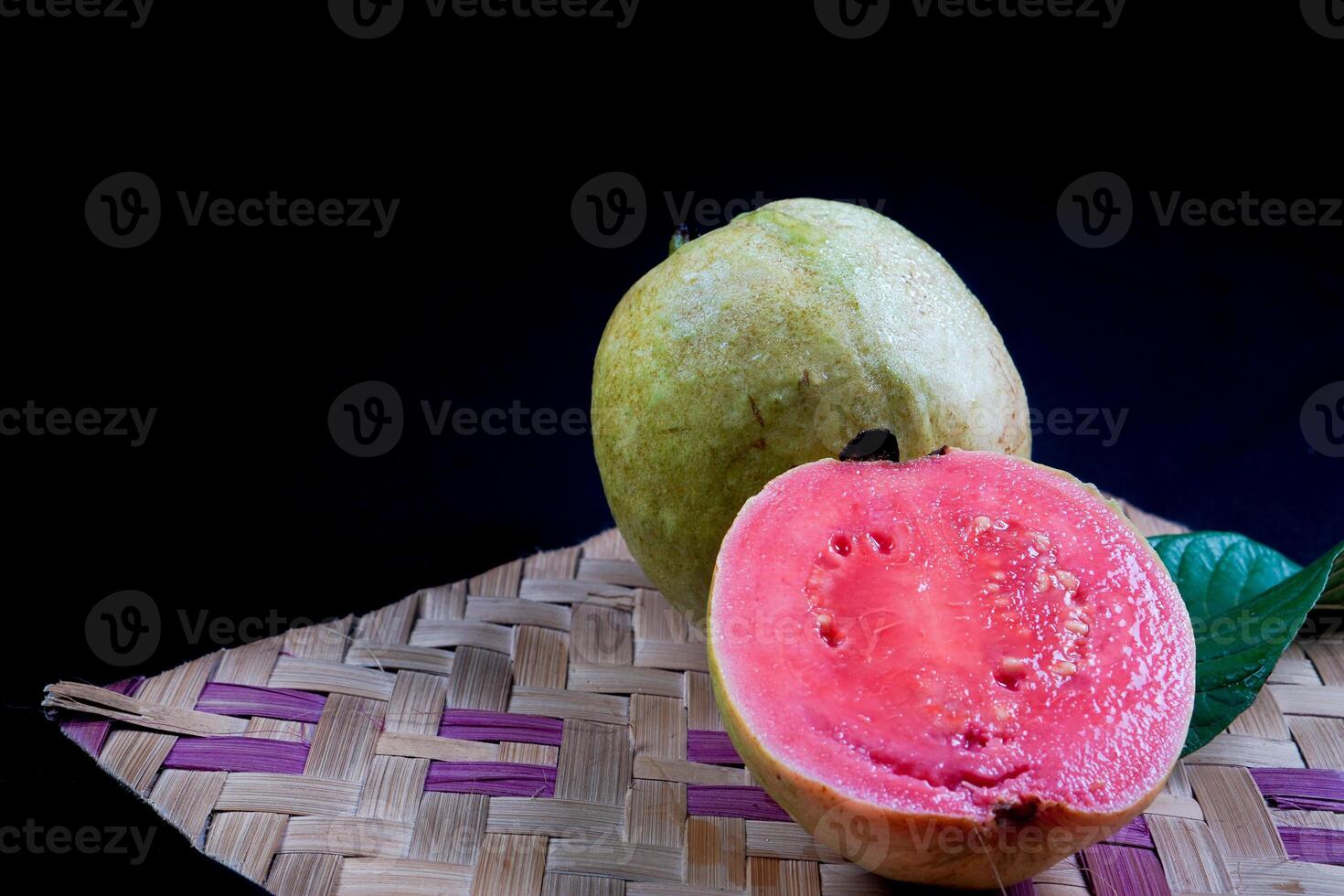 Guava isolated. Collection of red fleshed guava fruit with yellowish green skin and leaves isolated on black background with woven bamboo. photo