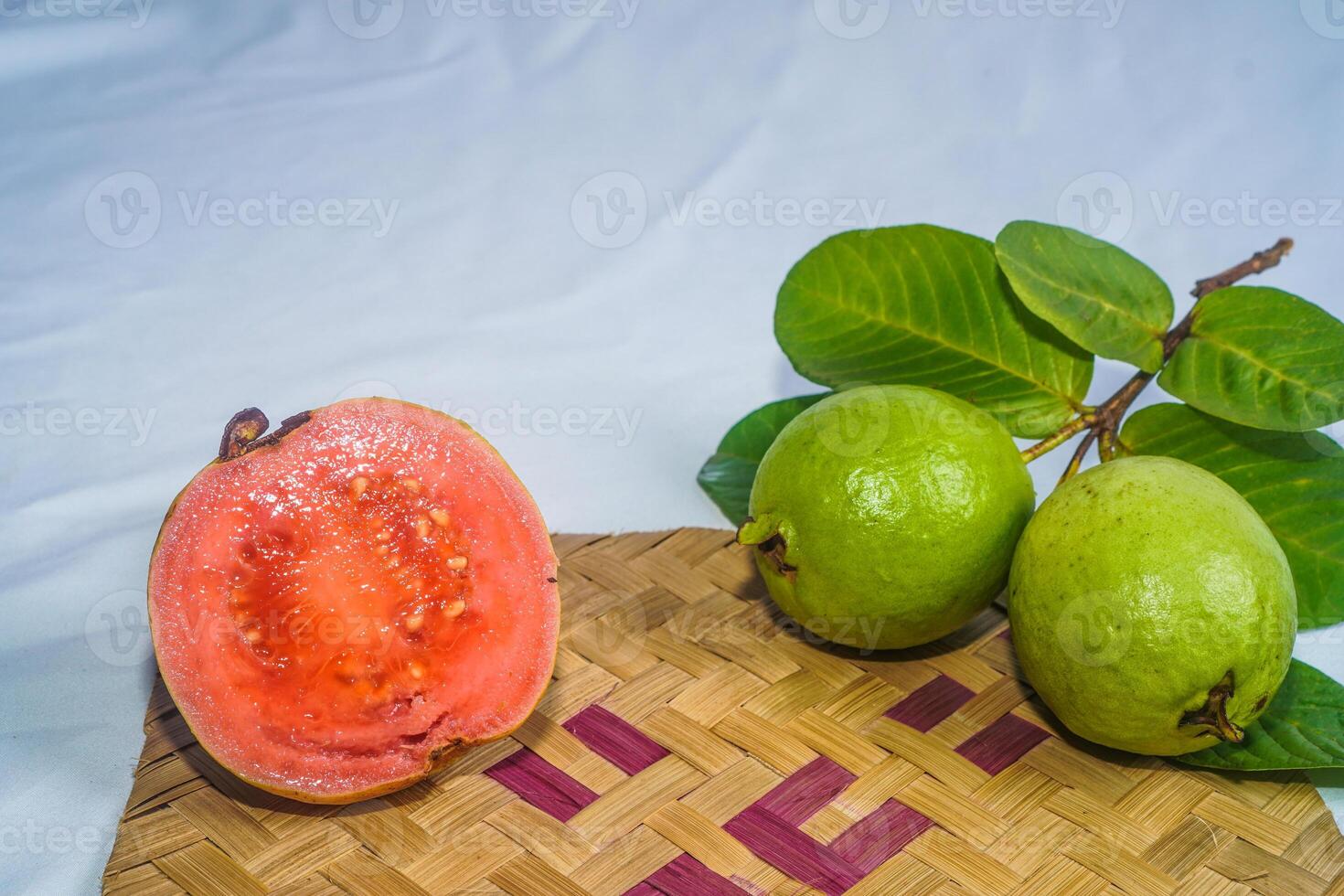 Guava isolated. Collection of red fleshed guava fruit with yellowish green skin and leaves isolated on a white background with bamboo matting. photo