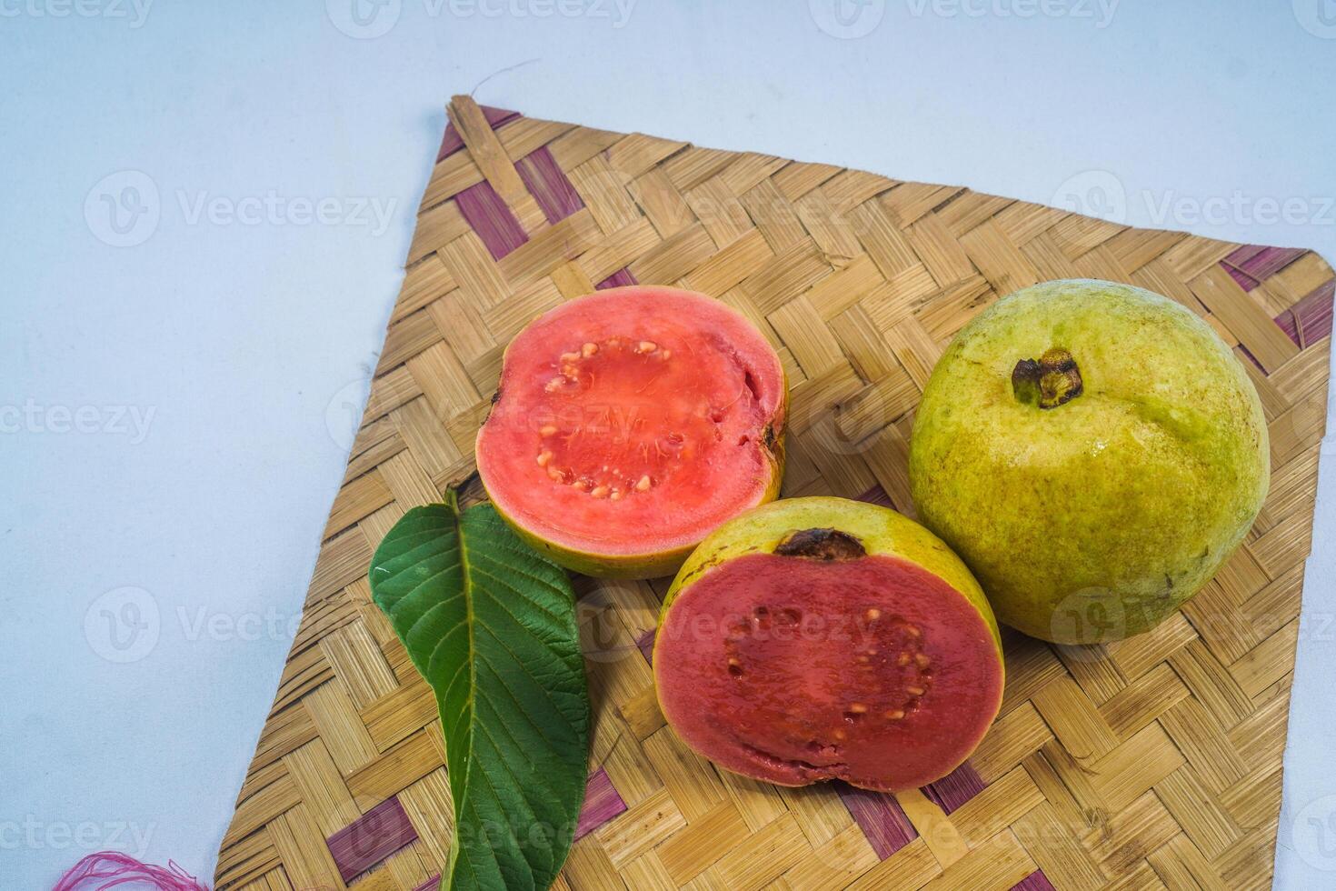 Guava isolated. Collection of red fleshed guava fruit with yellowish green skin and leaves isolated on a white background with bamboo matting. photo