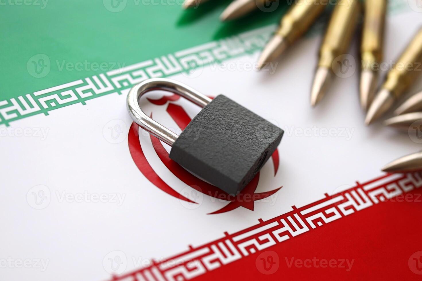 Small padlock lies on pile of iranian flag and rifle bullets close up. Sanctions, ban or embargo due to armed terror photo