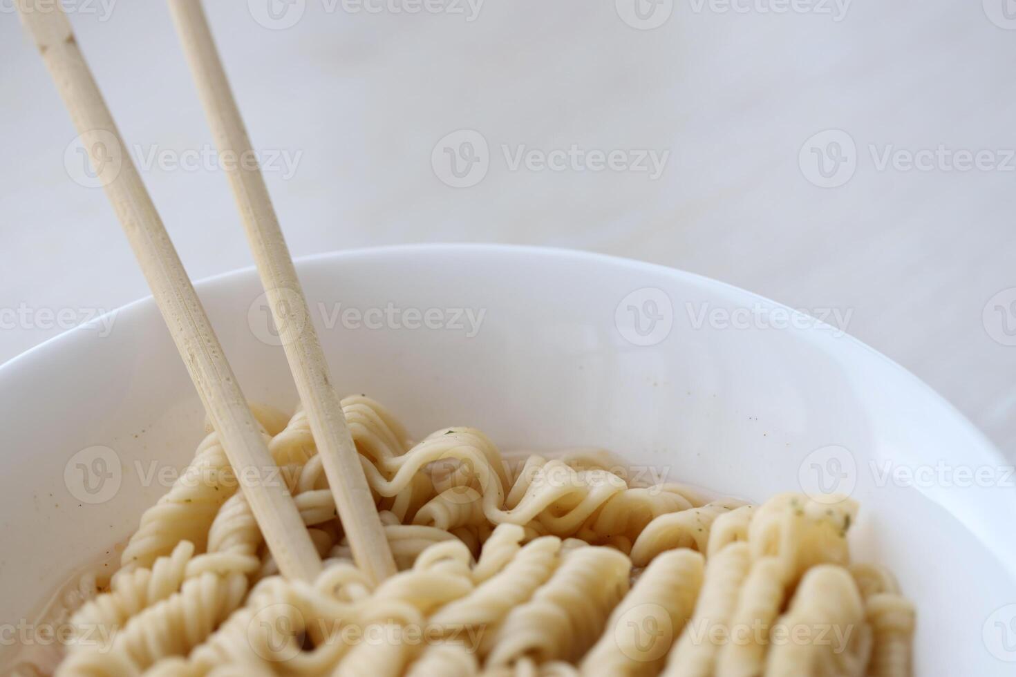 Bowl of instant cooking noodles with wooden chopsticks on white wooden table photo