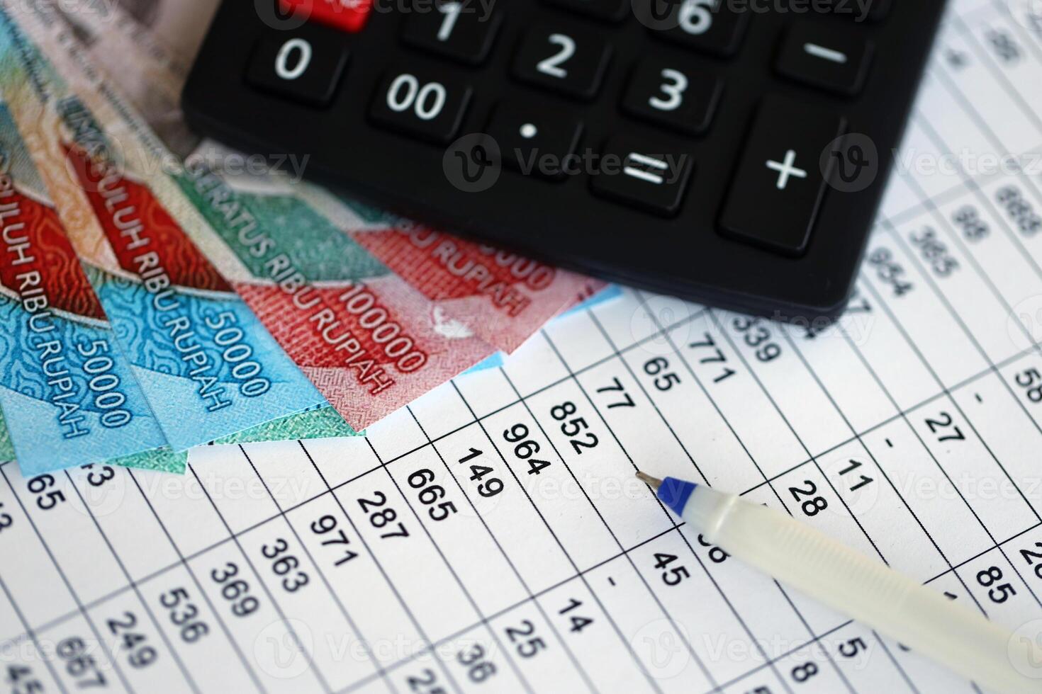 Business calculations with indonesian rupiah money bills and calculator with pen on office table photo