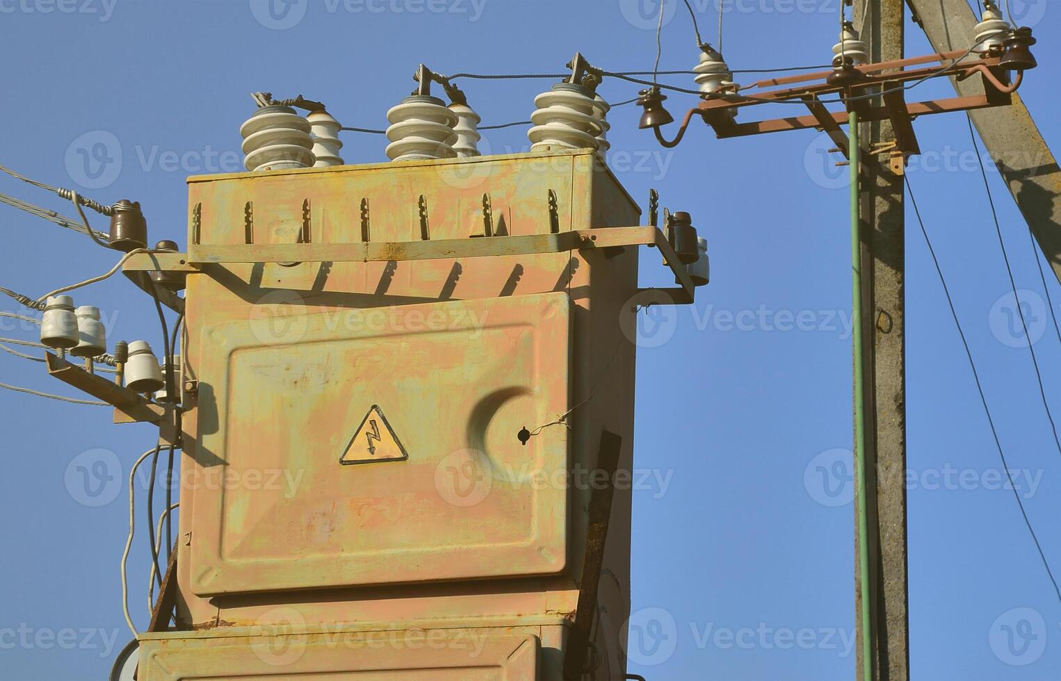 Old and obsolete electrical transformer against the background of a cloudless blue sky. Device for distribution of supply of high-voltage energy photo