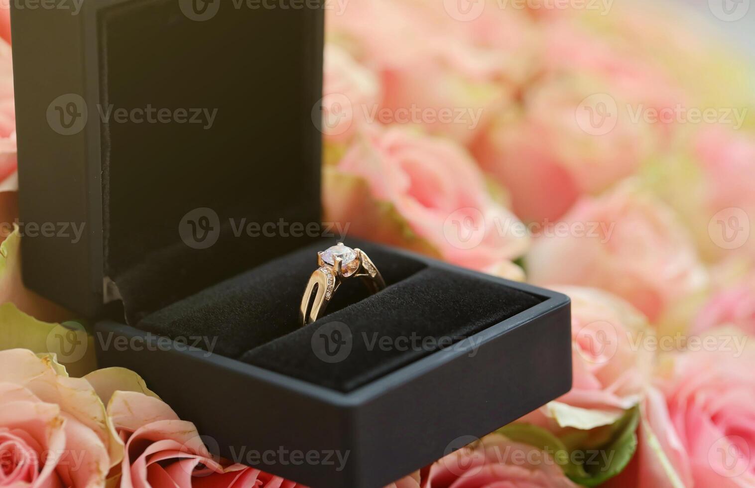 Gold diamond engagement ring in black box case among big amount of roses in big bouquet close up photo