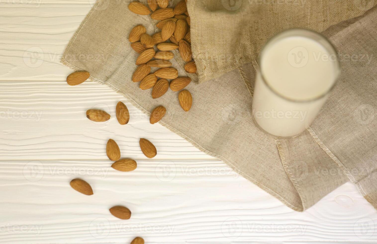 Glass of almond milk with almond nuts on canvas fabric on white wooden table. Dairy alternative milk for detox, healthy eating and diets photo