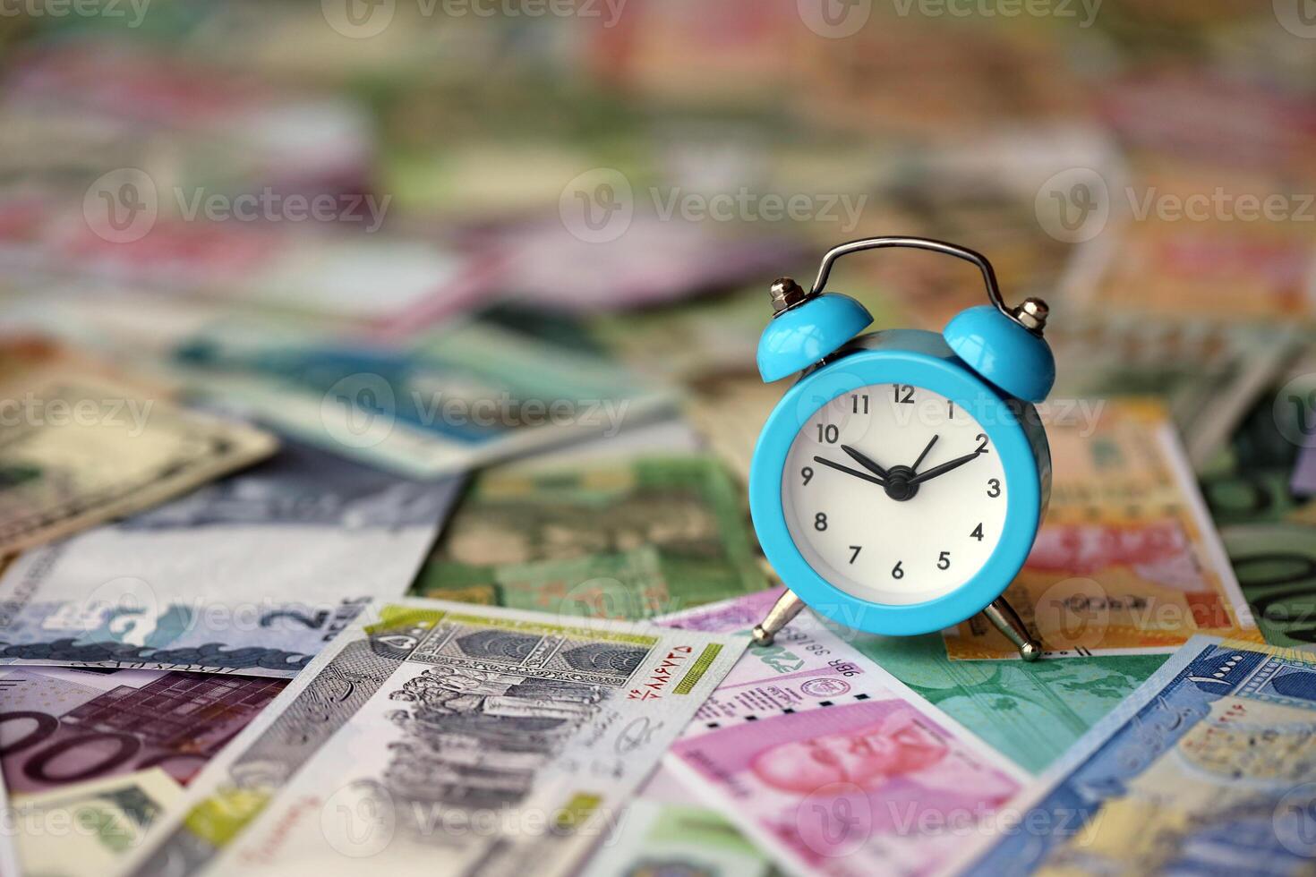 pequeño alarma reloj en muchos billetes de diferente divisa. antecedentes de hora y dinero foto