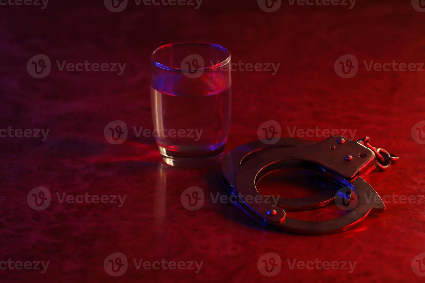 Handcuffs and glass of vodka alcohol drink. Concept of alcohol addiction or criminal photo