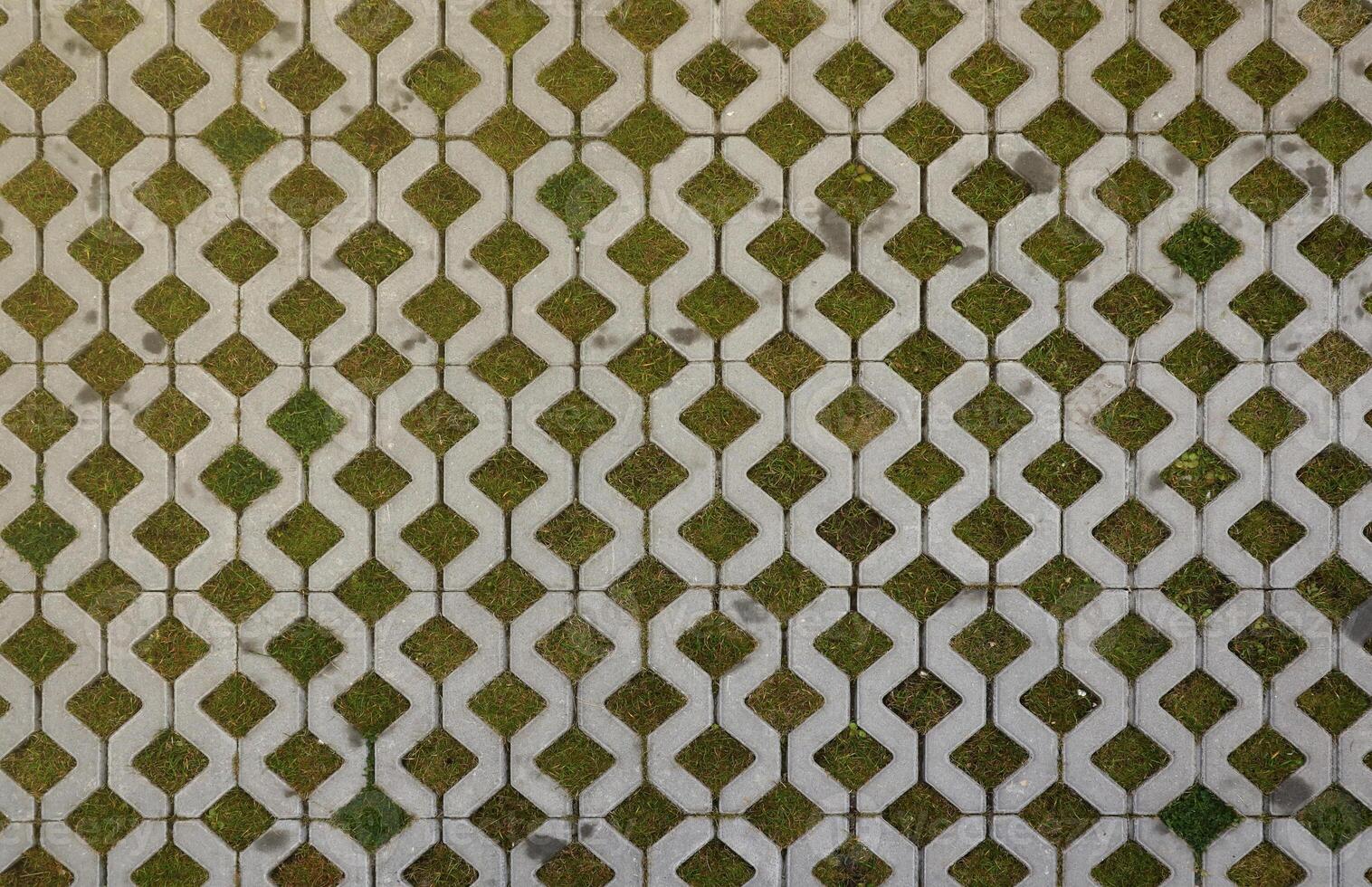 Geometric background of eco floor bricks and green grass. Eco parking texture. Floor stone tile with a rhomb hole for grass. Eco-friendly parking of concrete cells photo