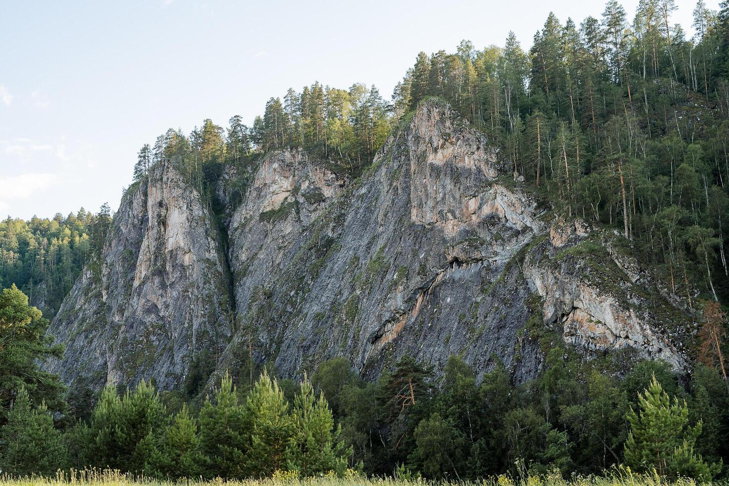 A pointed mountain peak overgrown with pine forest, hilly mountains, a landscape of gray rocks, a taiga forest of wildlife. photo