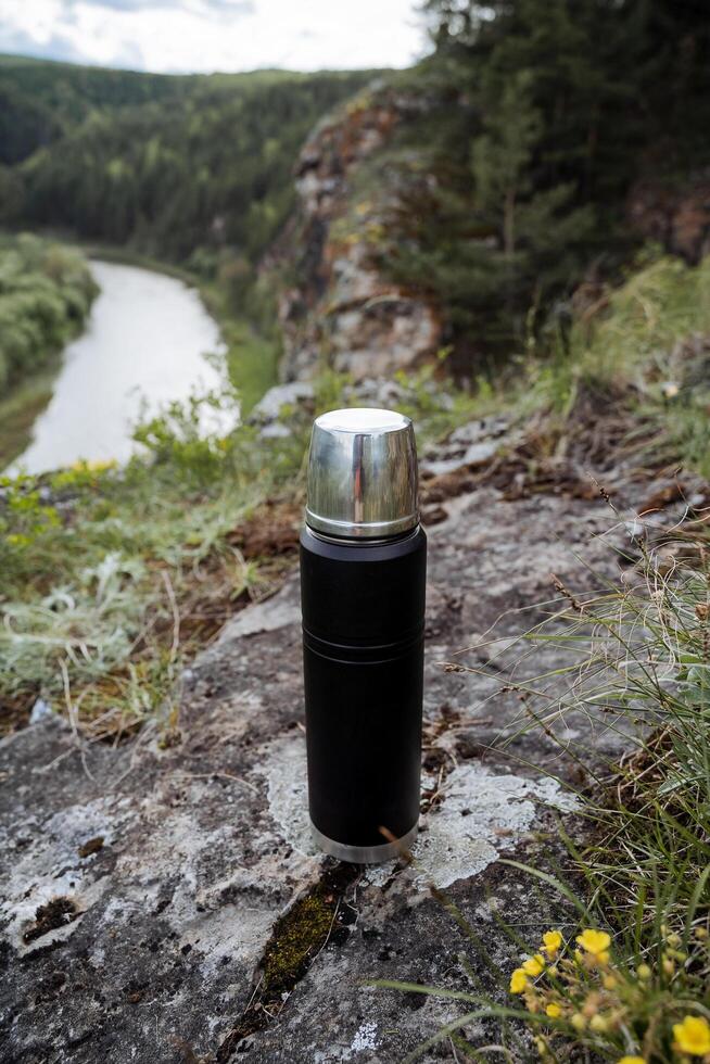 A thermos of hot coffee shot close-up, a black vacuum bottle for hot drinks. photo