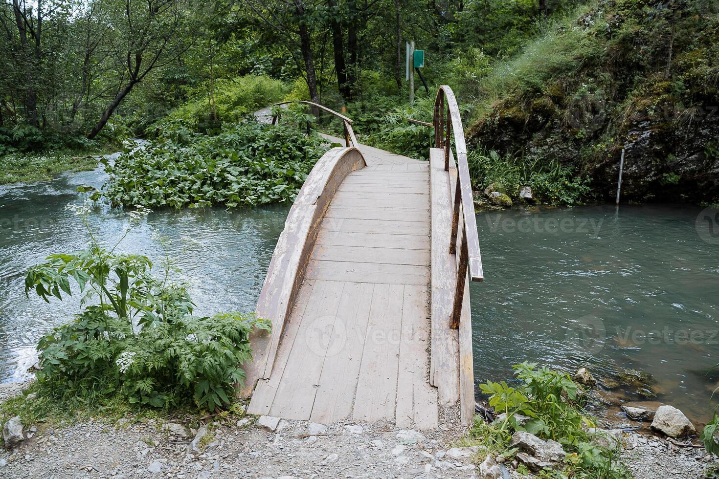 A wooden bridge of boards is thrown across the river, a mountain stream, a capital reliable bridge, a tourist trail, trekking in the forest, a recreation park. photo