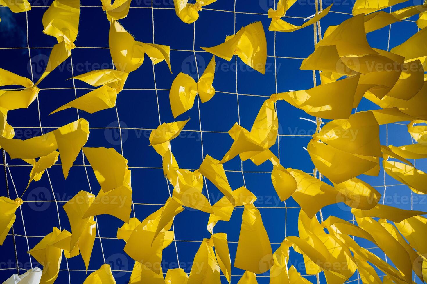 The concept of the flag of Ukraine in yellow blue colors, yellow ribbons hang on a grid against the background of the blue sky, decoration on top, a canvas of their fabric cut into pieces. photo