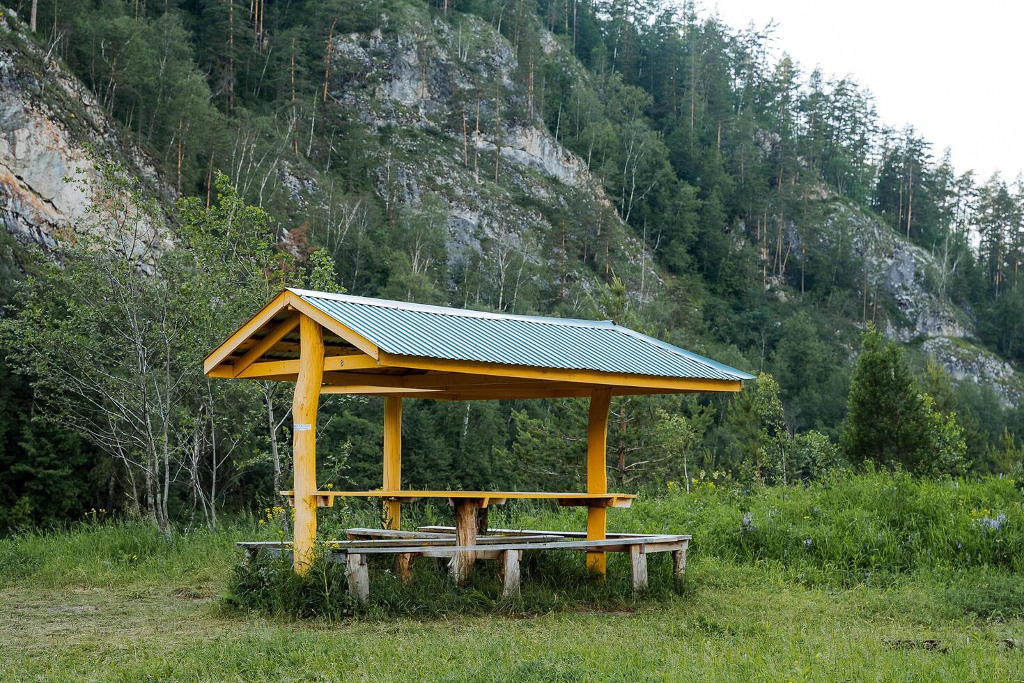 Table in the campsite with a canopy from the rain, a place to relax in nature, a parking lot equipped in the forest, a tourist camping under the mountain. photo