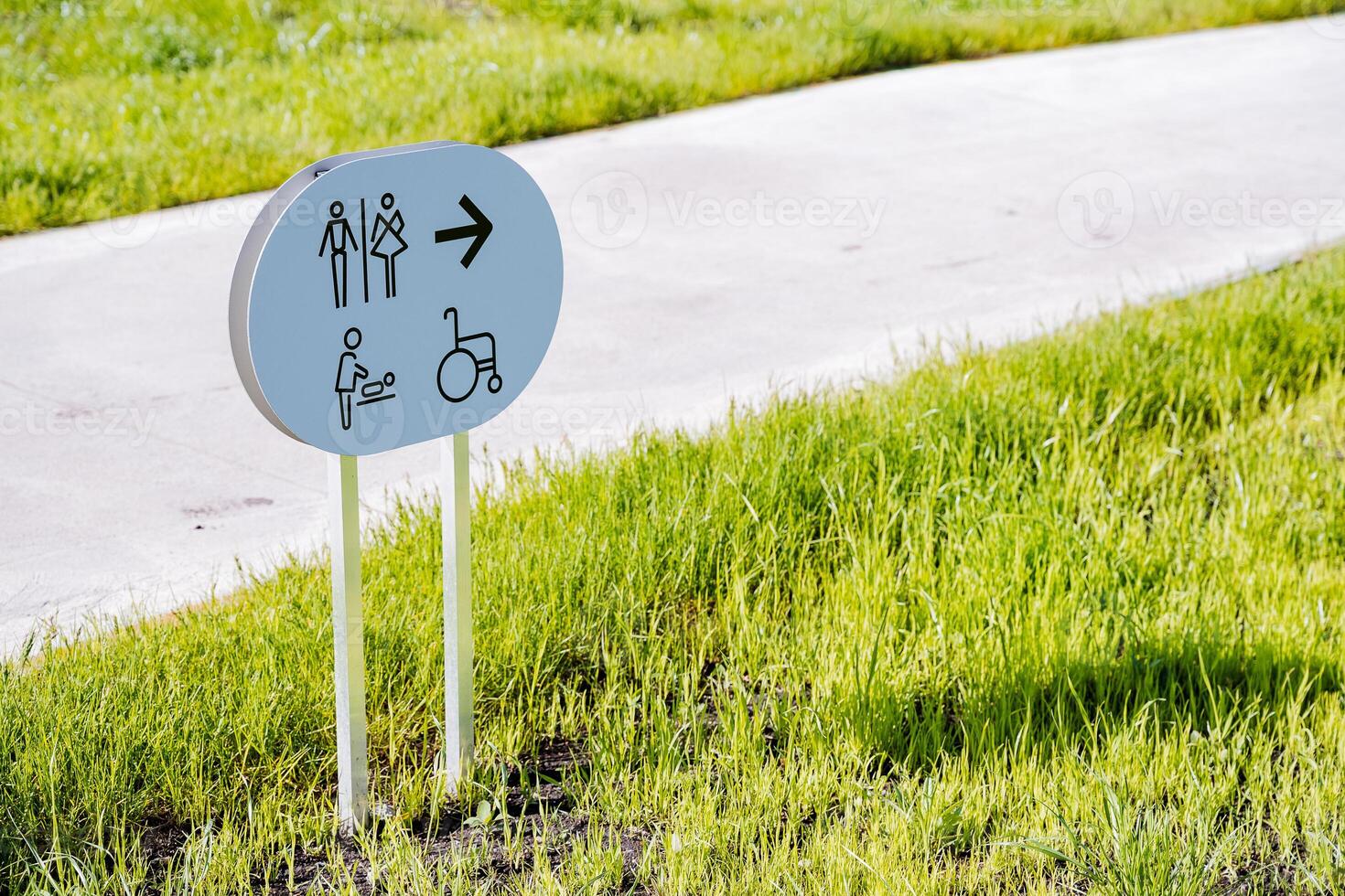 firmar con un flecha hacia el baño, un público Area de aseo para el desactivado, un madre e hijo habitación, un césped bandera, un ciudad baño, un la carretera en el parque. foto