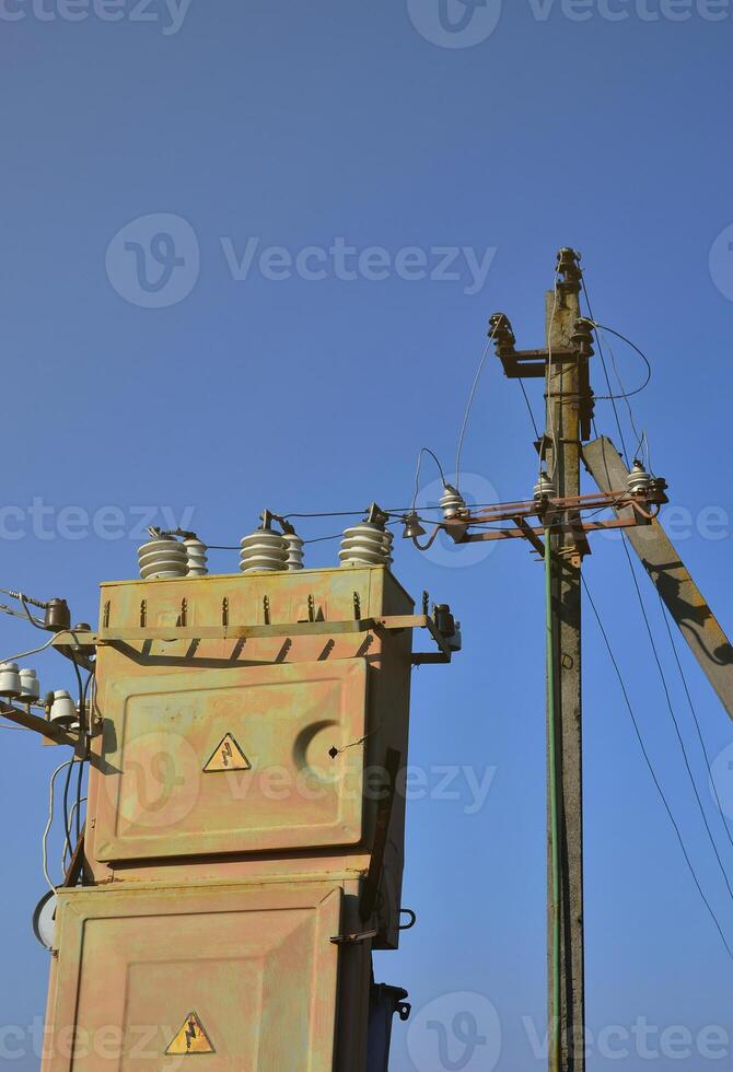 Old and obsolete electrical transformer against the background of a cloudless blue sky. Device for distribution of supply of high-voltage energy photo
