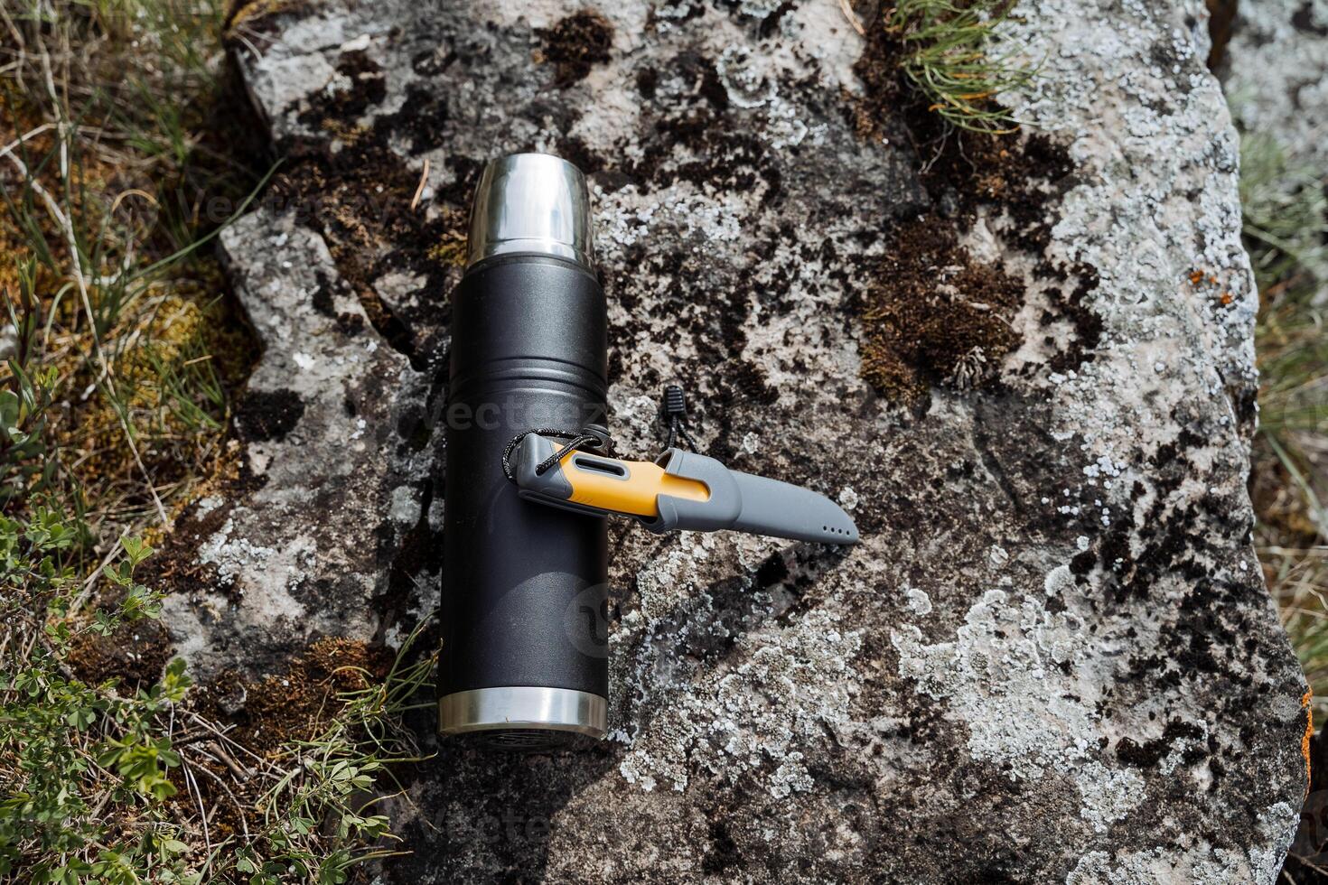 A thermos with tea for a trip to the forest, a warming drink poured into a thermo bottle, a hiking knife for cutting bread, camping equipment. photo