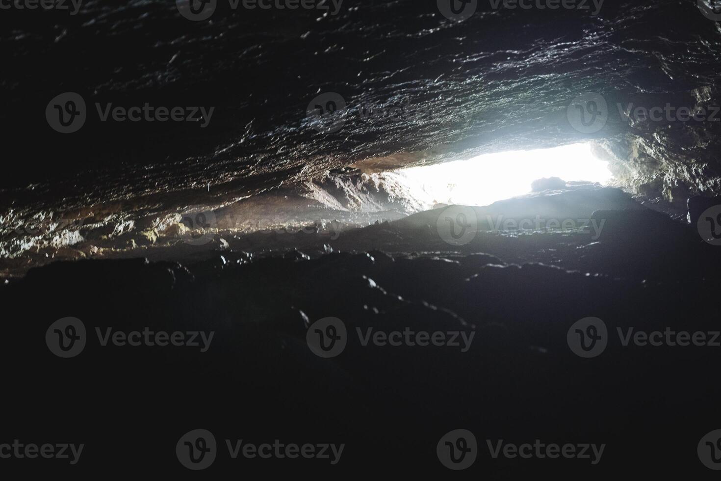 Cave light at the end of the passage, narrow underground manhole, overhanging vaults of the cave grotto, bright spot of light, speleology in section. photo