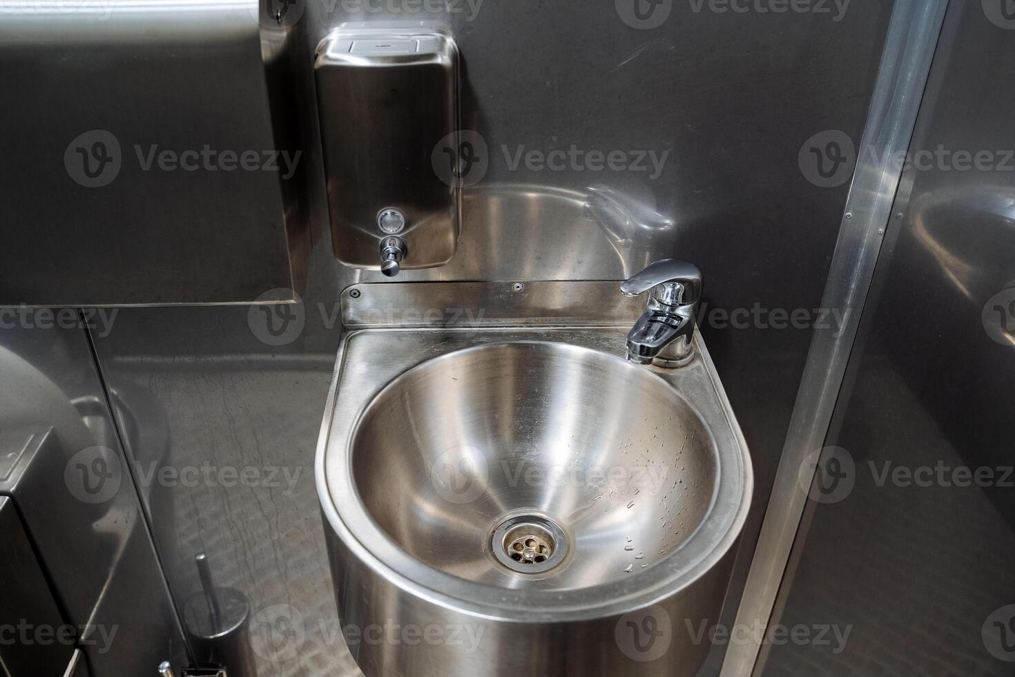 Stainless steel metal sink, soap dispenser, small faucet, hand sink, anti-vandal washbasin, public toilet in the city. photo