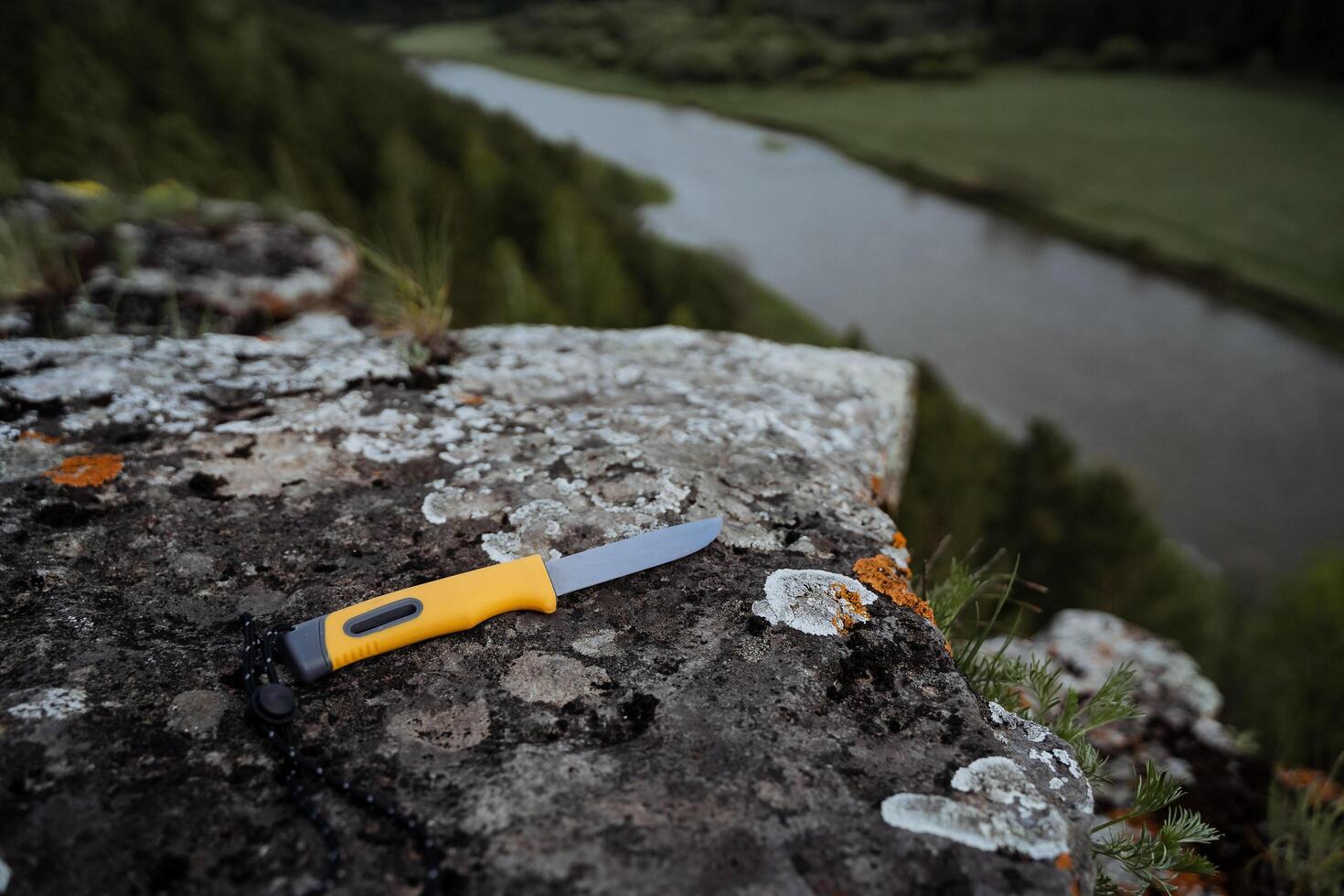 A knife with a plastic yellow handle lies on a stone. Blade for cutting in a hike, camping equipment element. photo