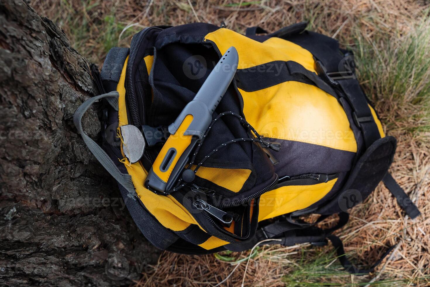 A hiking knife for survival in the forest lies on a backpack, a hiking knife with a yellow handle, gray plastic sheath, a lanyard for the hand. photo