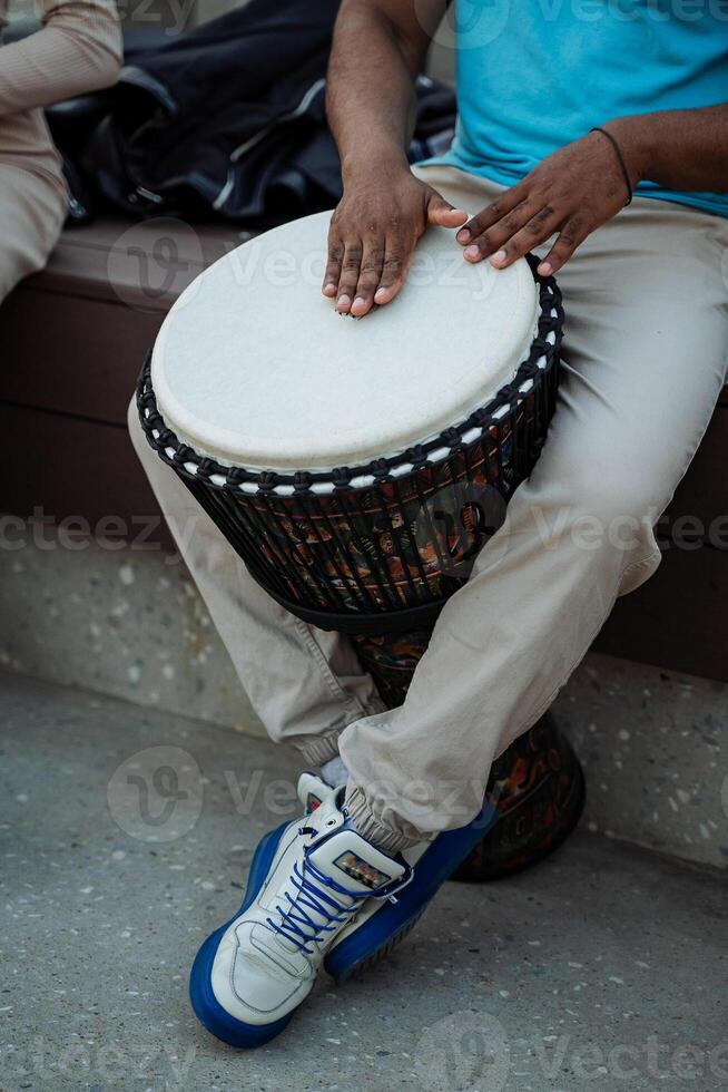 un negro chico extractos el sonidos de un tambor con un puñetazo, un calle músico tambores entre el multitud, un africano obras de teatro el ritmos de el tribu. foto