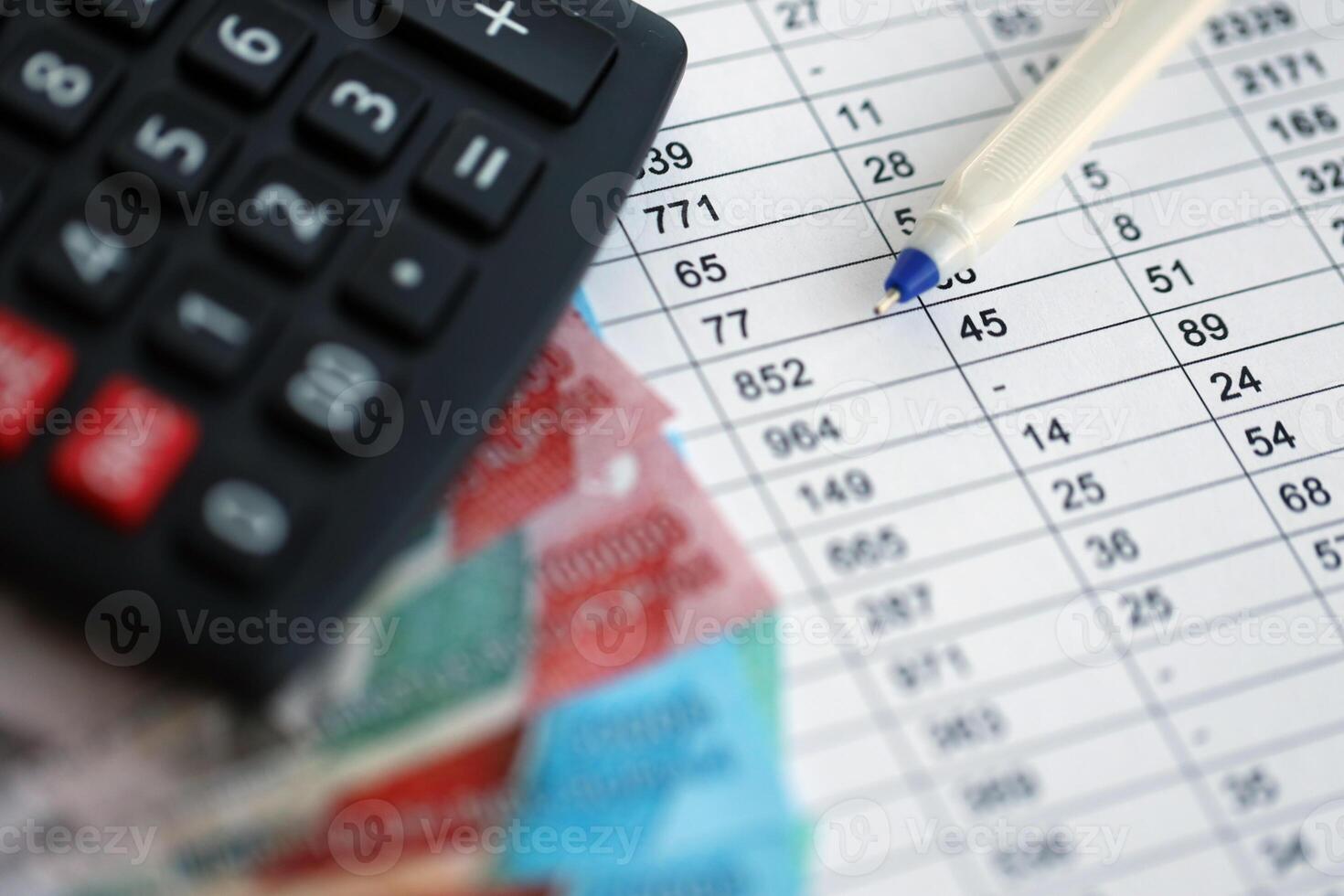 Business calculations with indonesian rupiah money bills and calculator with pen on office table photo