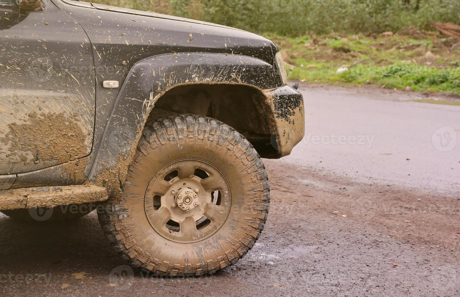 Wheel closeup in a countryside landscape with a mud road. Off-road 4x4 suv automobile with ditry body after drive in muddy road photo