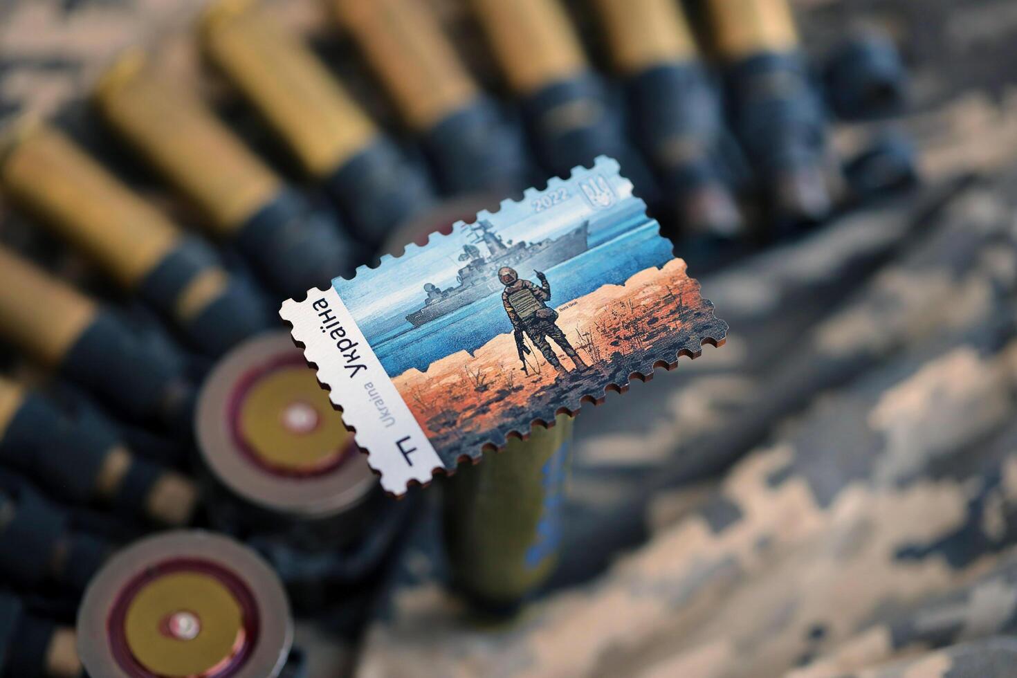 TERNOPIL, UKRAINE - SEPTEMBER 29, 2023 Famous Ukrainian postmark with russian warship and ukrainian soldier as wooden souvenir on army camouflage uniform cloth and machine gun belt photo