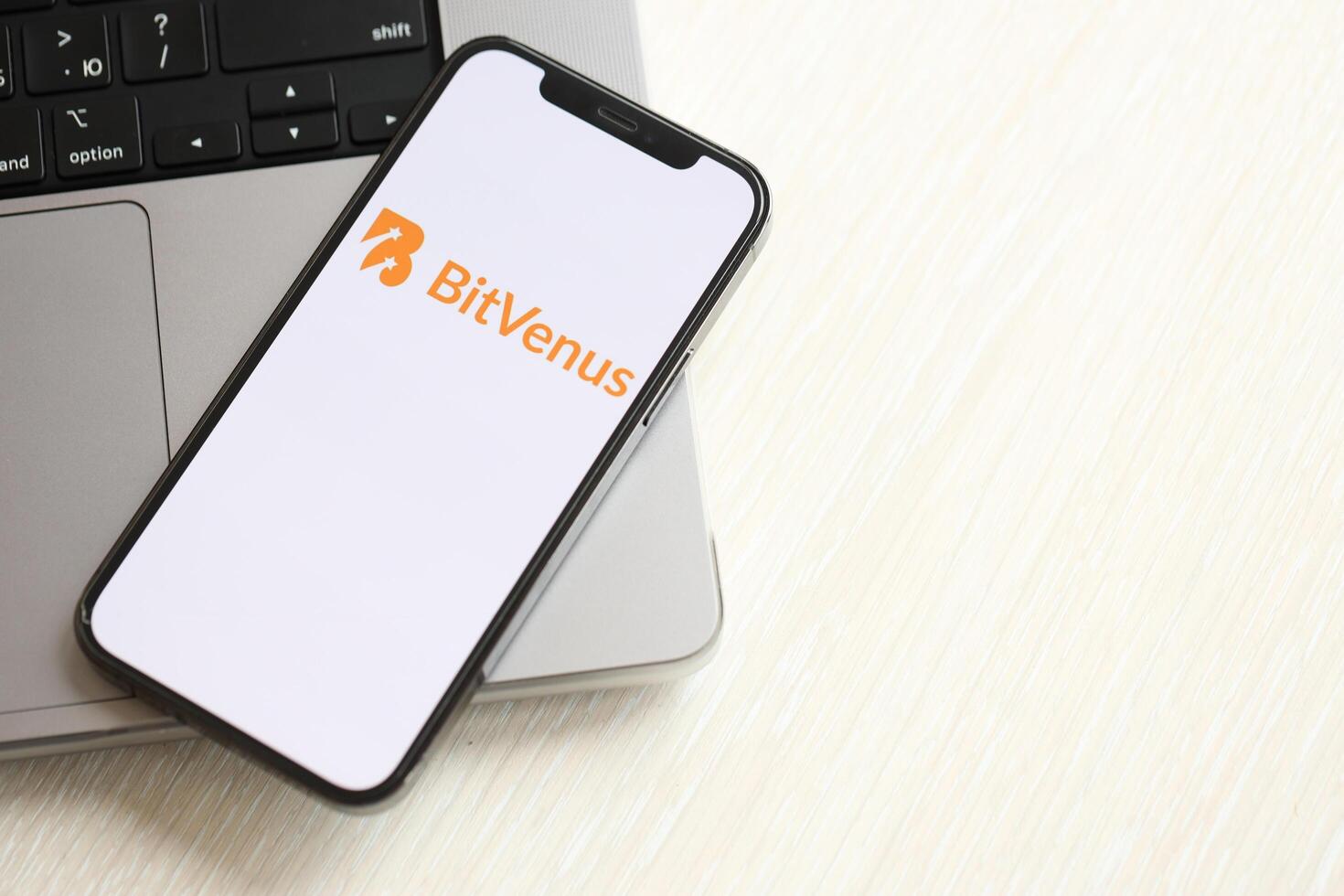 KYIV, UKRAINE - MARCH 15, 2024 Bitvenus logo on iPhone display screen on MacBook panel logo on iPhone display screen with dollars and bitcoins on MacBook photo
