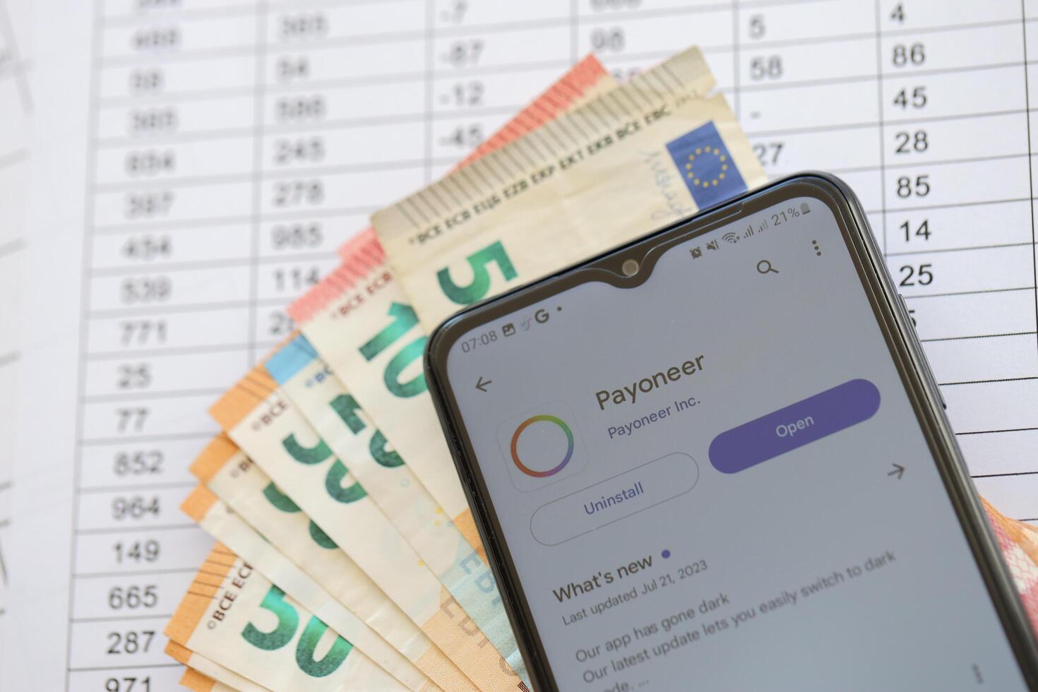TERNOPIL, UKRAINE - AUGUST 3, 2023 Payoneer application on screen on modern smartphone and many bills of euro currency photo
