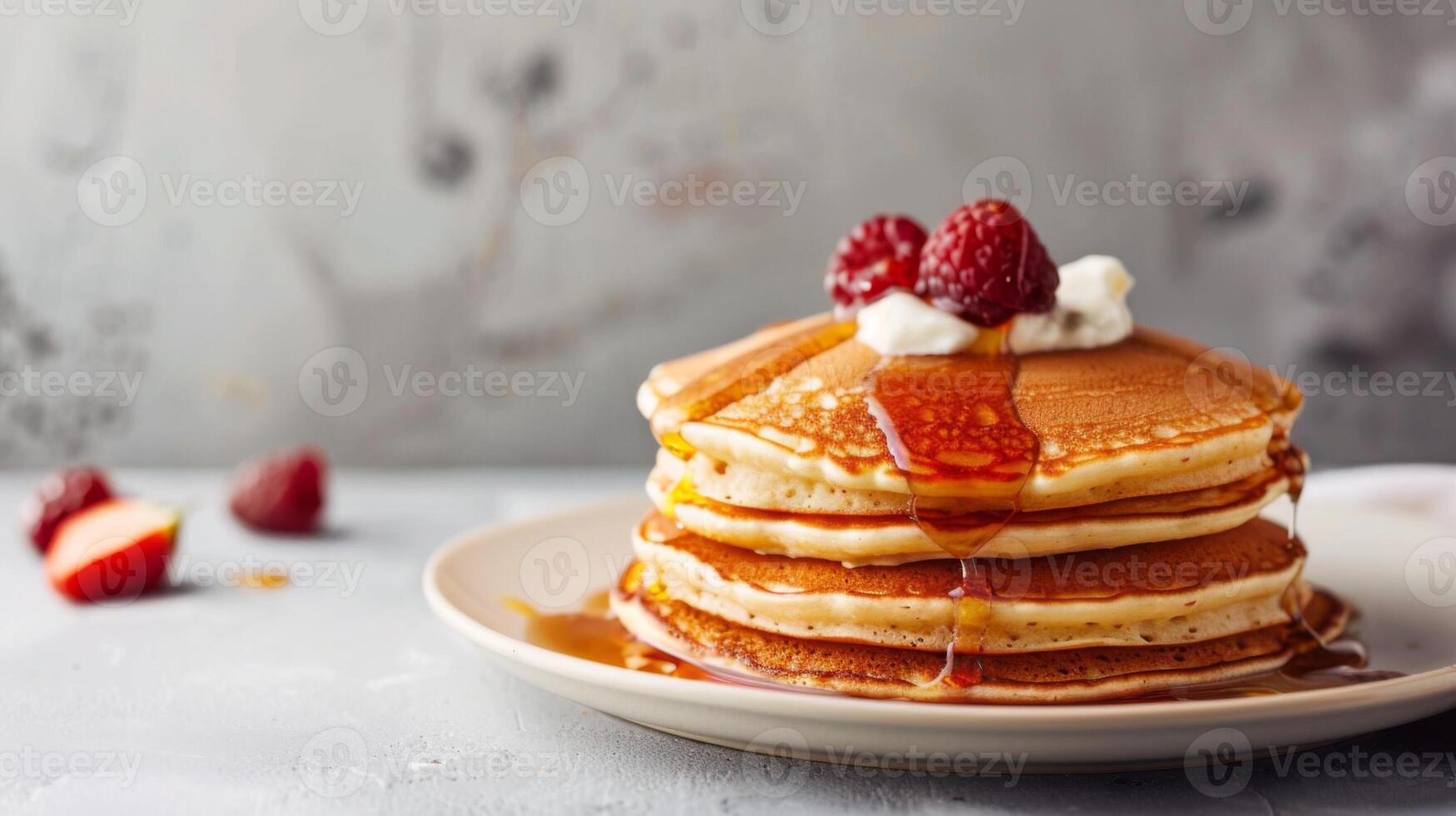 Stack of pancakes dripping with syrup and topped with raspberries and cream for a sweet breakfast treat photo