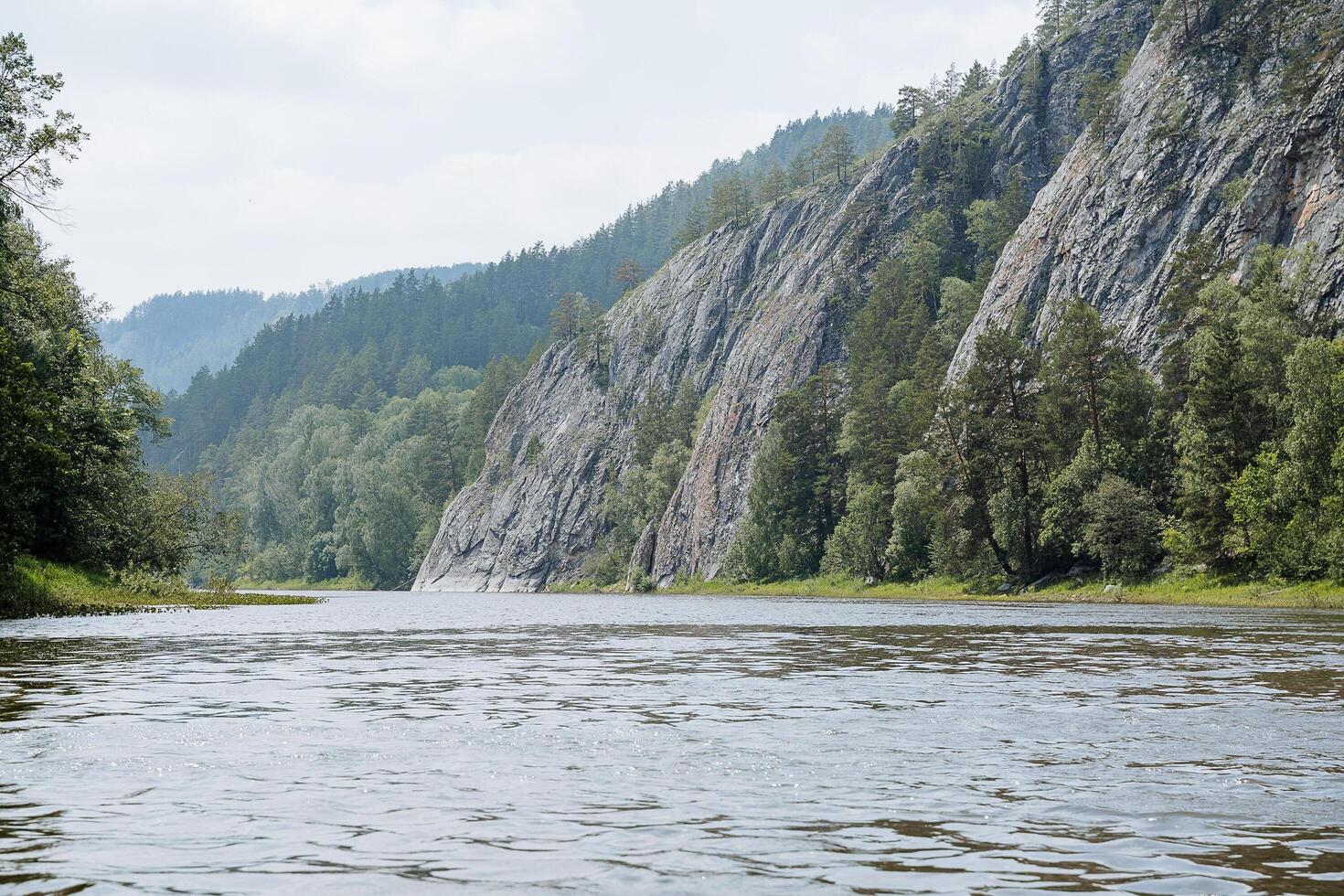 The water surface on the wild taiga river, the panorama of the mountain river, the sheer cliffs near the water, the nature reserve, the hot day, the beautiful landscape, the mountains and the forest. photo