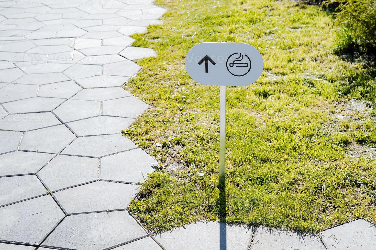 Arrow pointer on the banner smoking area, cigarette painted on a white sign, pedestrian zone, information stand on the lawn. photo