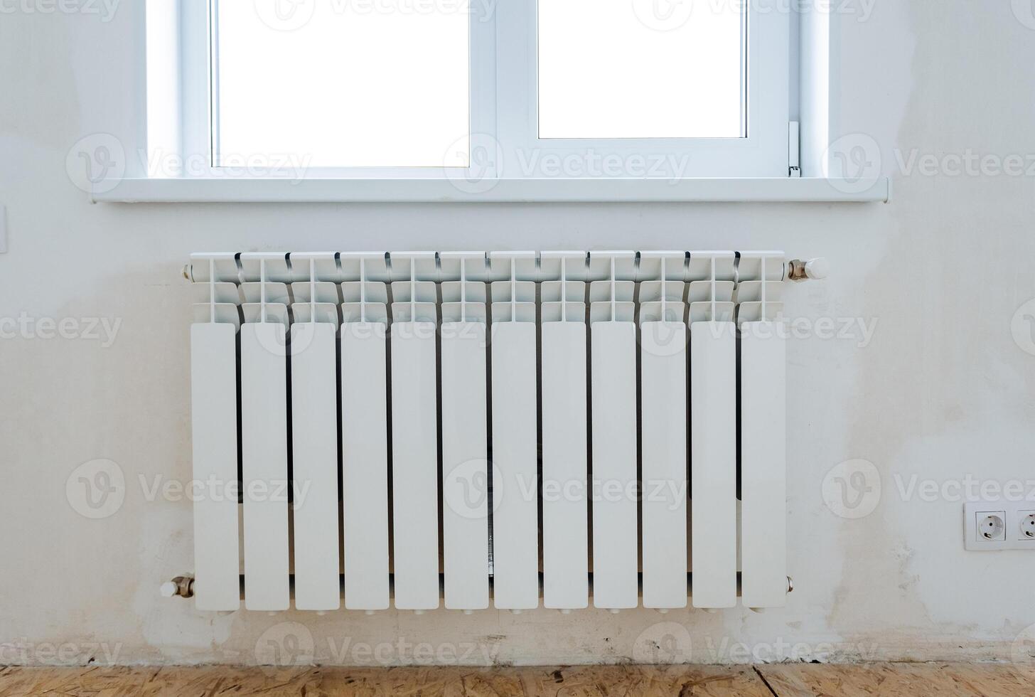 A thermal radiator hangs on the wall under the window, a house heater is a heat convector in winter, a white metal apartment heater. photo