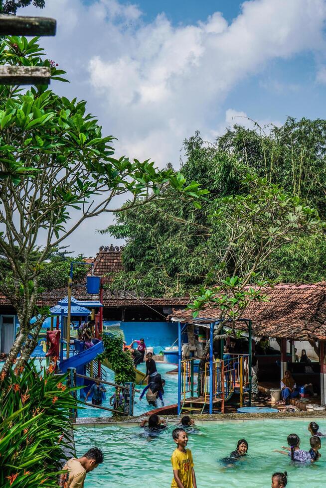 Jepara, Central Java, April 14, 2024 - Swimming pool rides surrounded by trees are full of visitors during holidays. photo