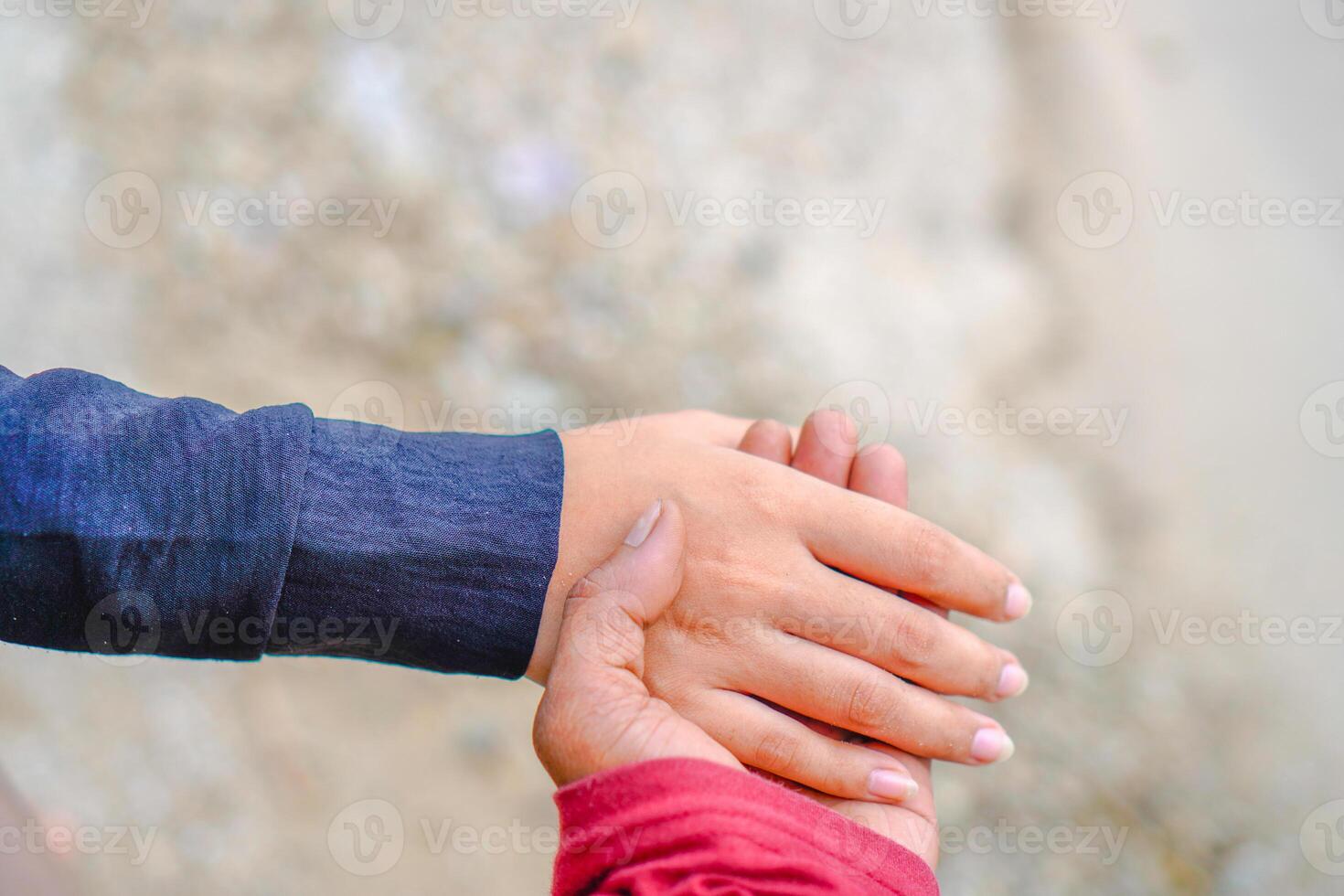 the hands of a couple holding hands against the background of beach sand. photo