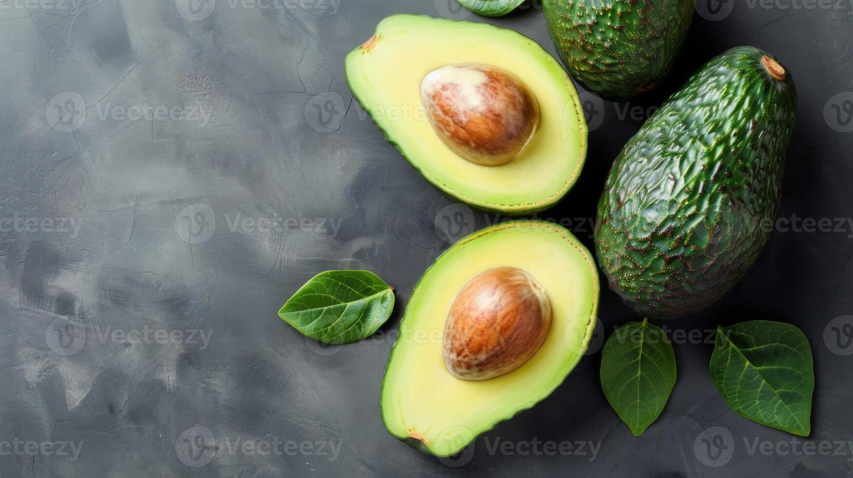 Ripe avocado halves with a seed and a whole fruit on a dark textured background photo