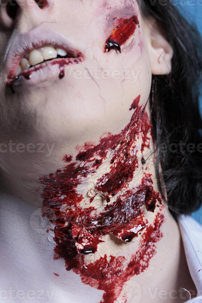 Extreme close up shot of bloody injury on woman neck acting as zombie for horror film scene. Gore undead corpse scars with fake blood achieved through professional SFX makeup for Halloween costume photo