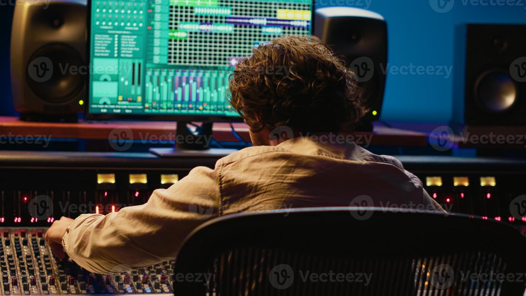 Cheerful energic audio engineer dancing on his own music creation in professional studio, editing a recording on mixing console and daw software. Sound designer processing tracks. Camera A. photo