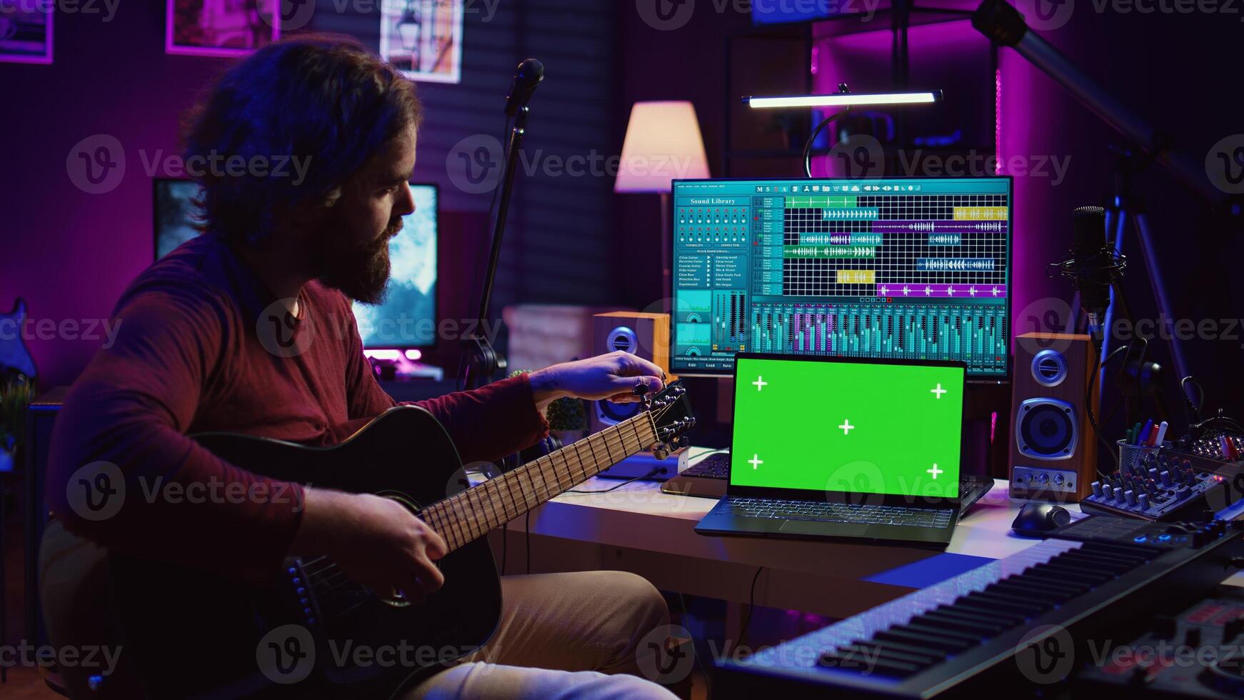 Musician learning to play new acoustic instrument in his home studio, practicing online guitar lessons on isolated greenscreen display. Watching tutorial on laptop to develop his skills. Camera B. photo