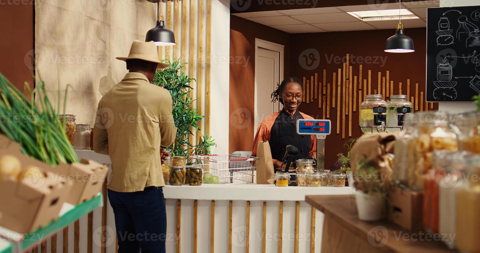 African american seller working at supermarket cash register counter, weighting organic additives free fruits and vegetables. Vendor selling fresh bio produce to male customer at checkout. Camera 2. photo