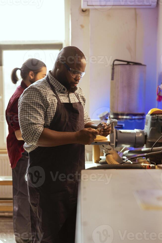 African american carpenter looking at screwdriver, preparing to start production in furniture assembly shop. BIPOC cabinetmaker at workbench inspecting tool, ready to work on wood designs photo