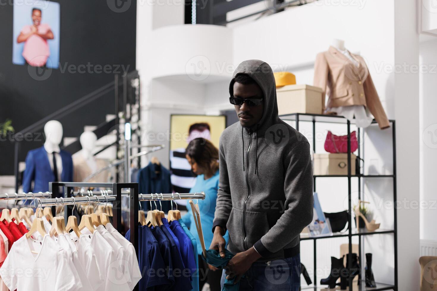 African american thief trying to robbing shopping mall, looking at hangers full with fashionable clothes. Robber looking around before taking casual t-shirt in modern boutique. Burglary concept photo