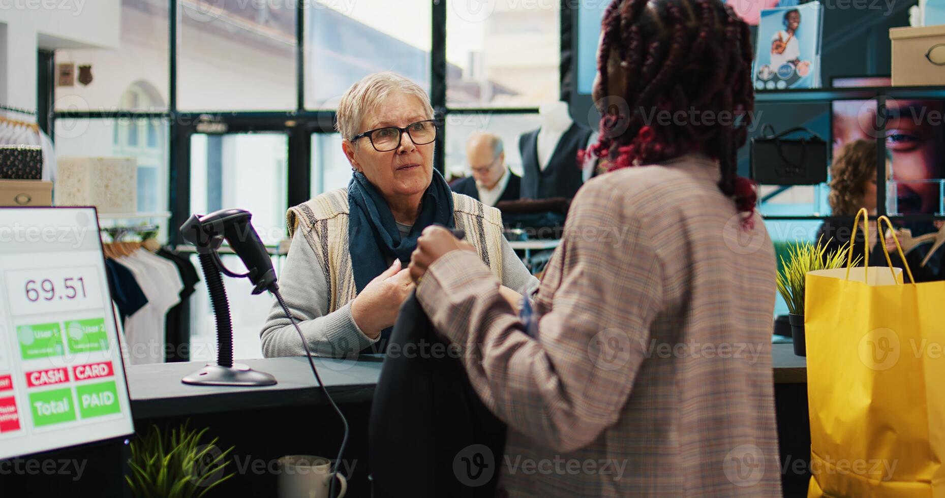 African american employee scanning clothes tags at checkout, preparing bag with products for elderly woman at department store. Retail worker using scanner at cash register, consumerism. Camera B. photo