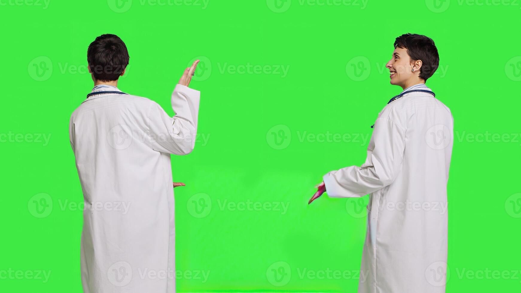 Physician pointing to the left or right to create web commercial standing against greenscreen backdrop, doing a marketing advertisement in studio. Woman medic in white coat shows an ad. Camera B. photo