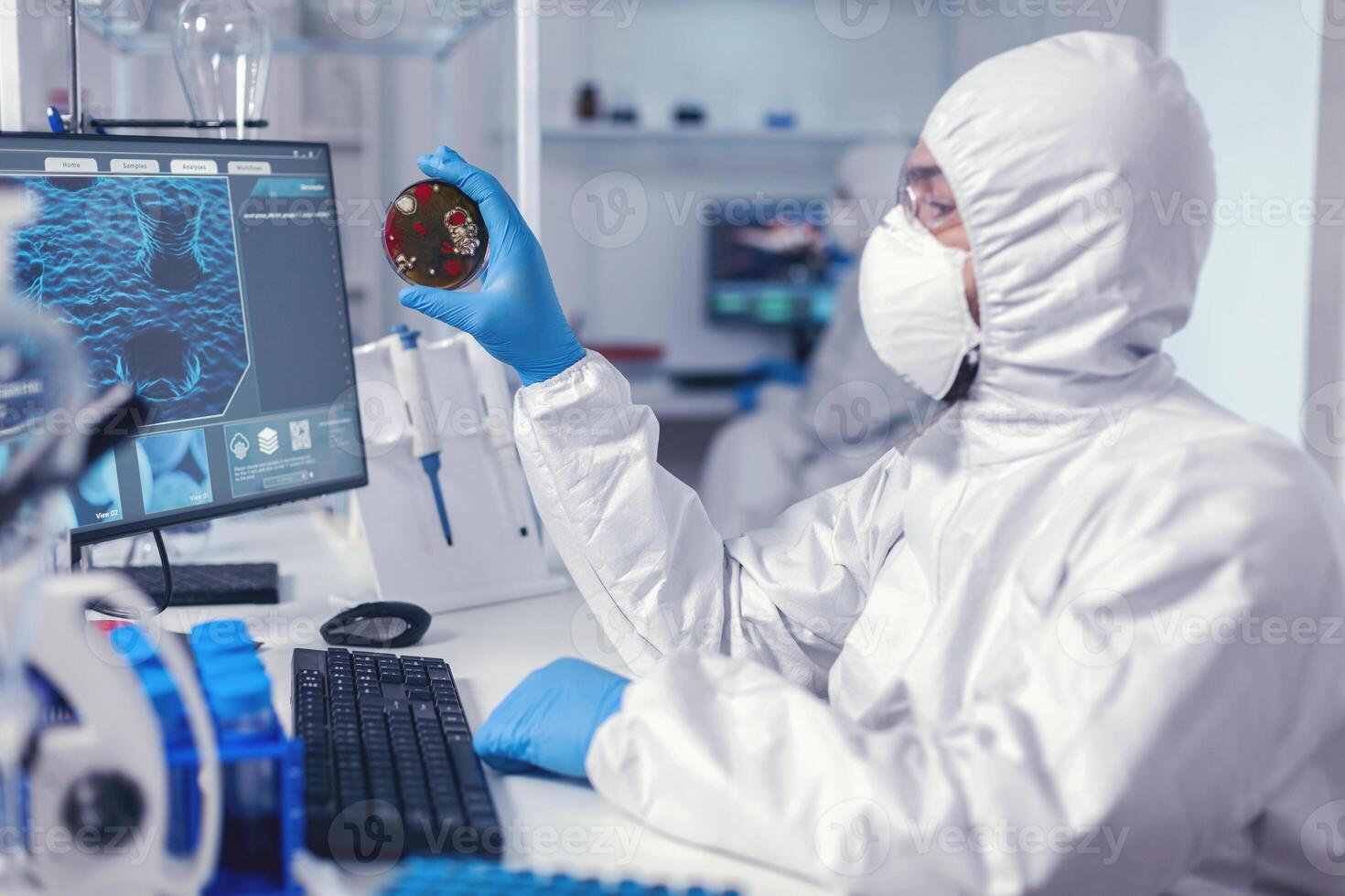 científico examinando solución en petri plato en laboratorio vestido en ppe traje. doctores analizando vacuna evolución utilizando alto tecnología investigando diagnóstico en contra covid19 virus. foto