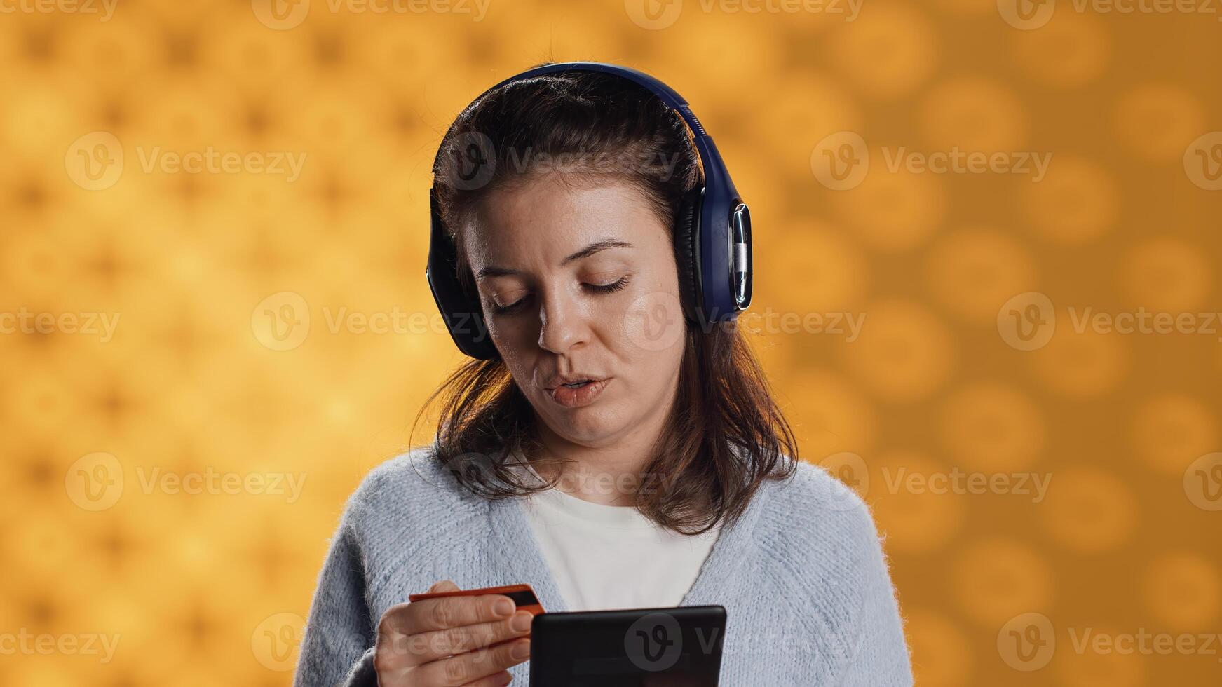 Woman reading ebook on ereader and listening music purchasing books online. Person with tablet looking to buy digital novel with credit card, hearing songs in headphones, studio background, camera A photo