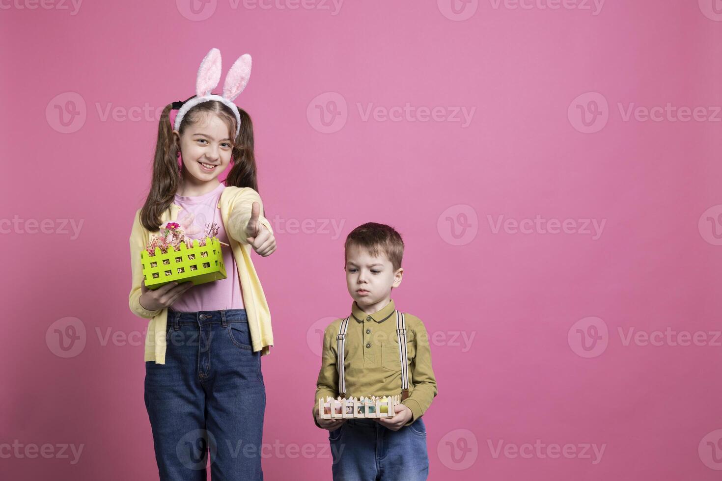 Joyful siblings feeling happy celebrating easter holiday and spring time, little girl giving thumbs up on camera. Brother and sister showing baskets filled with painted eggs and decorations. photo