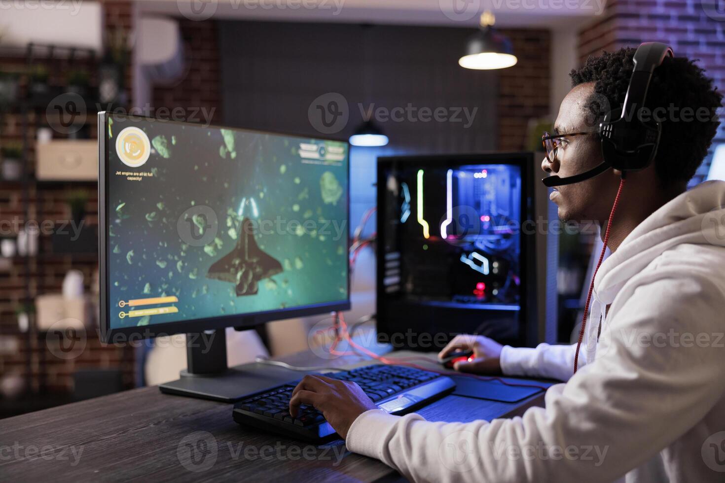 Gamer playing classic arcade action game, flying through space debris. African american man enjoying leisure time at home using high tech gaming PC to solve missions in singleplayer game photo