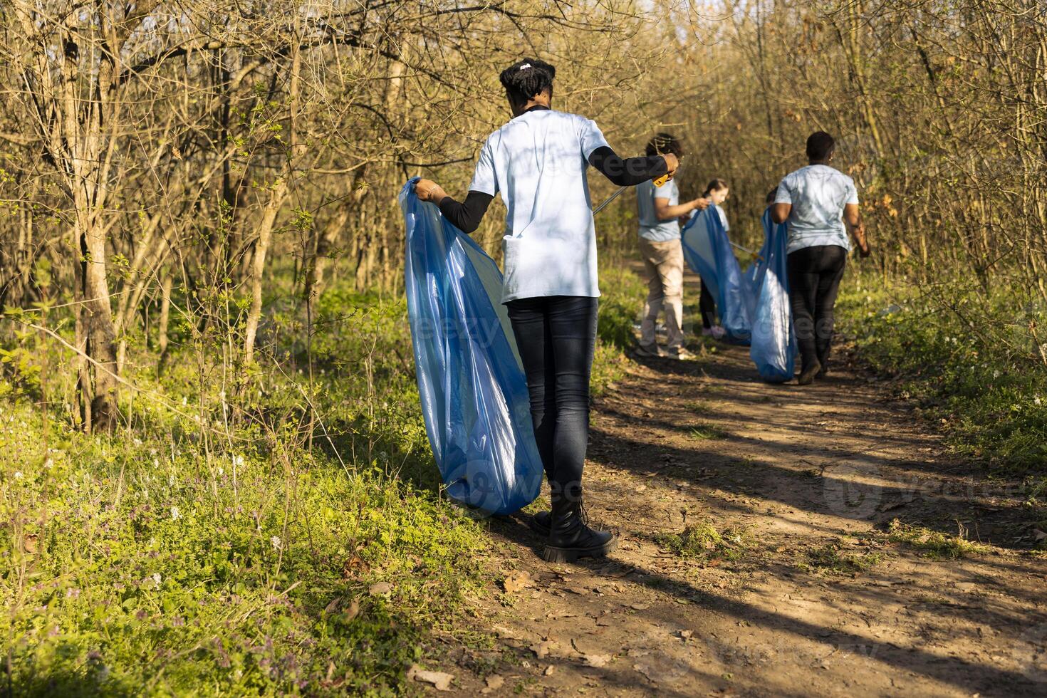 African american climate change volunteer grabbing trash in a bag, working to protect the natural environment. Volunteering for nature conservation and community service action. photo